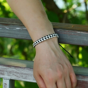 Close-up of hand-woven black and white checkered leather bracelet with adjustable drawstrings