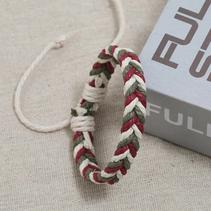 Detail of red and green hand-woven adjustable rope bracelet on a textured beige background