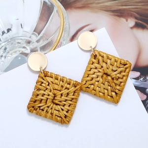 Gros plan sur des boucles d'oreilles en rotin tissé carré avec clous dorés sur carte