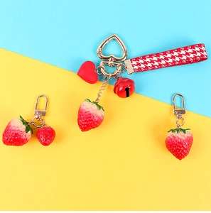 Macro detail of strawberry keychains with houndstooth ribbon and golden bells on colorful background