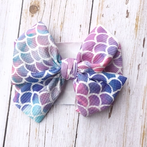 Mermaid scale print infant headband with oversized bow on white wood background