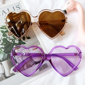 Detail shot of heart-shaped sunglasses in tea and purple tint on a soft fabric backdrop
