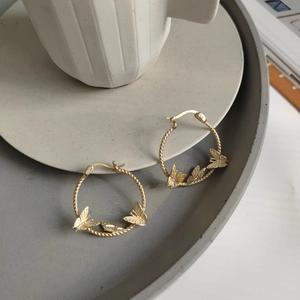 Macro detail of gold S925 sterling silver hoop earrings with butterfly charms