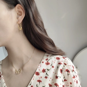Detailed shot of golden geometric hollow pendant and textured twisted hoop earrings