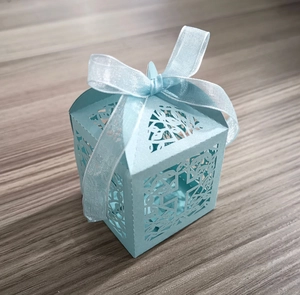 Close-up of laser-cut light blue wedding candy box with floral patterns and ribbon