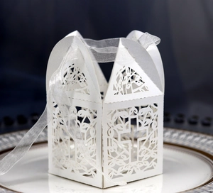 Close-up of laser-cut white favor box with cross design and white organza ribbon