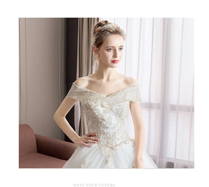 Detailed view of white off-the-shoulder wedding gown with intricate gold lace embroidery