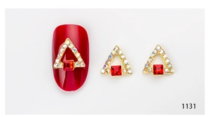 Macro detail of triangle 3D nail art charm with red square crystal and gold rhinestones