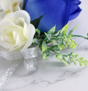 Detail van een corsage met koningsblauw en witte zijden rozen met glanzend zilveren lint voor bruid