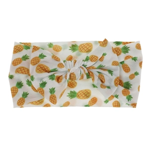 Detail view of a white nylon baby headband with vibrant pineapple print and a bow knot