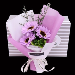 Macro shot of purple artificial sunflower bouquet in a striped gift box with a white ribbon