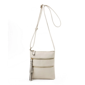 Detailed view of cream crossbody bag featuring triple zip pockets and tassel charm