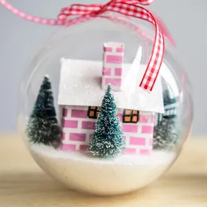 Clear Christmas ornament ball with a miniature pink house and snowy trees inside