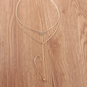 Collier double couche doré avec pendentif cœur et chaîne en Y sur surface en bois