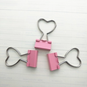 Detailed view of three pink heart-shaped binder clips on lined paper office background