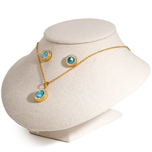 Golden jewelry set featuring light blue crystal pendant and matching stud earrings on a bust