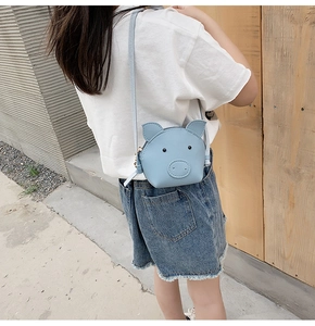 Blue cartoon pig crossbody bag shown on a young girl model in a stylish outdoor setting