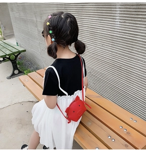 Rear view of a girl carrying a cute red pig-shaped crossbody bag on a wooden bench