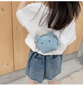 Detail of a light blue cartoon pig shoulder bag worn by a child on a bright background