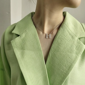 Silver H-letter pendant necklace with shimmering zircon stones worn with a green blazer