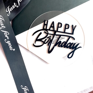 Macro detail of round transparent acrylic cake topper with 3D black Happy Birthday text