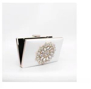 Detail of white evening clutch with large sparkling rhinestone sunflower ornament and gold frame