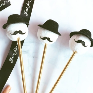 Close-up of three creative cake toppers with white pompom, black mustache and top hat details