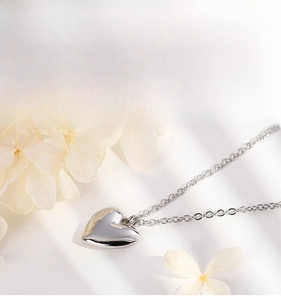 Vue détaillée d'un collier pendentif coeur poli avec chaîne fine sur tissu blanc