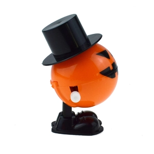 Close-up of wind-up walking pumpkin toy with black hat and white knob for Halloween