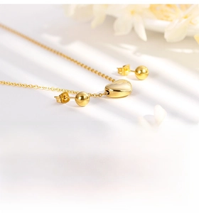 Macro detail of gold stainless steel heart pendant necklace and ball stud earring set