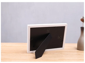 Rear view of white wooden photo frame with black fiberboard and dual mounting hooks
