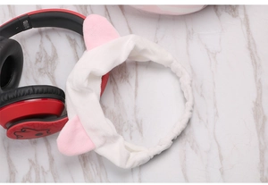 Close-up of white plush cat ear headband on marble background with headphones