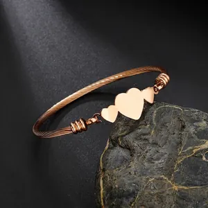 Détail du bracelet torsadé en or rose avec trois breloques métalliques en forme de cœur