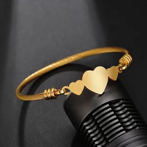 Gros plan détaillé d'un bracelet jonc doré avec trois cœurs et un design torsadé