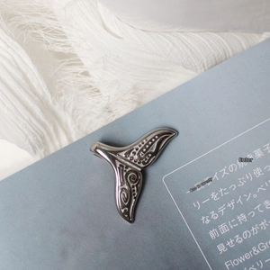 Vintage style stainless steel whale tail pendant with detailed texture on book pages