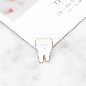 Close-up of a creative cartoon tooth enamel pin with a cute smile on a white marble background