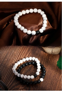 Close-up of white howlite and matte black agate beaded bracelets on satin and wood