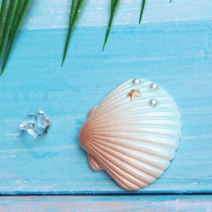 Macro detail of large resin seashell with pearls and golden starfish on blue wood