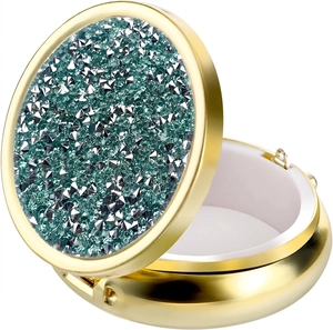 Detail of portable gold pill box with sparkling green crystals and white inner compartment