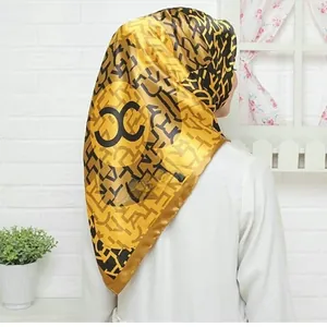Detail of a bright yellow silk-textured hijab featuring black geometric patterns