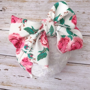 Elastic baby headband with pink rose print and large bow on a rustic wood background