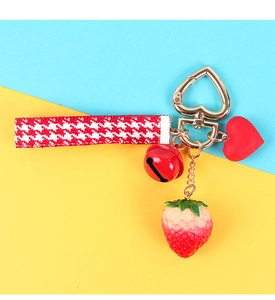 Detail of strawberry keychain with red bell, heart clasp, and plaid ribbon accessory