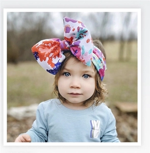 Close-up of a floral print baby headband with a large bow worn by a girl outdoors