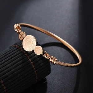 Macro shot of rose gold Saint Benedict medals on a twisted steel wire open bangle
