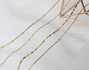 Detail of diverse gold plated titanium steel chains on soft white fabric background