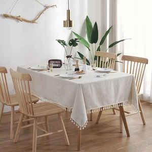 Close-up of beige linen tablecloth with elegant fringe on a wooden dining table