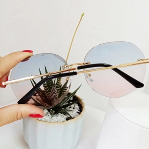 Detail of rimless polygon sunglasses with blue-pink gradient lenses and gold temples