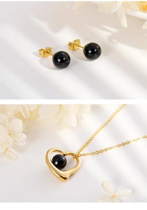 Detailed view of gold heart necklace with black bead and matching sphere stud earrings