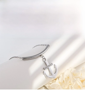 Détail du collier ancre argenté avec zircons sur un présentoir blanc aux lignes courbes