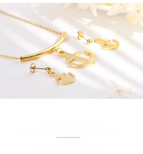 Macro shot of gold anchor pendant necklace and stud earrings set on a floral backdrop